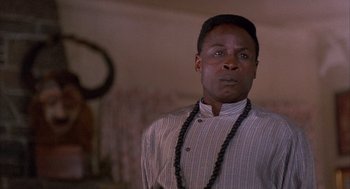 Movie still from “The Believers” (1987), directed by John Schlesinger – A man wearing a long necklace in front of a mirror; Close Up shot, Low angle