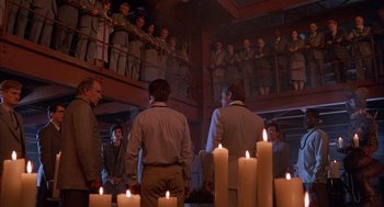 Movie still from “The Believers” (1987), directed by John Schlesinger – A group of people standing around a room with candles; Wide shot, High angle