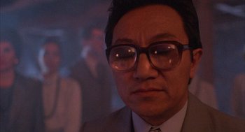 Movie still from “The Believers” (1987), directed by John Schlesinger – A person wearing a suit and glasses; Close Up shot, Low angle