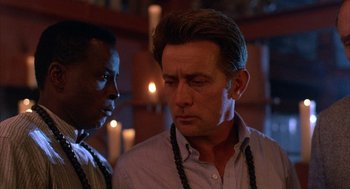 Movie still from “The Believers” (1987), directed by John Schlesinger – Two men standing next to each other in front of candles; Close Up shot, Over the shoulder angle