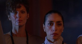 Movie still from “The Believers” (1987), directed by John Schlesinger – Two women standing next to each other in front of a wall; Close Up shot, Low angle