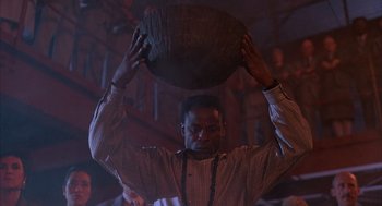 Movie still from “The Believers” (1987), directed by John Schlesinger – A man is holding a basket on his head; Medium shot, Low angle