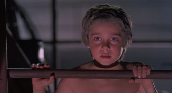 Movie still from “The Believers” (1987), directed by John Schlesinger – A young boy holding a wooden bar in a dark room; Close Up shot, Over the shoulder angle