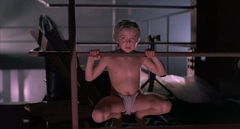 Movie still from “The Believers” (1987), directed by John Schlesinger – A young boy in underwear holding onto a bar; Medium shot, Low angle