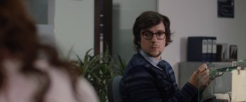 Movie still from “The Belko Experiment” (2016), directed by Greg McLean – A man with glasses sitting in front of a plant; Close Up shot, Over the shoulder angle