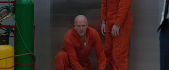 Movie still from “The Belko Experiment” (2016), directed by Greg McLean – A man in red is crouched down in front of a wall; Medium shot, Low angle