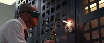 Movie still from “The Belko Experiment” (2016), directed by Greg McLean – A man wearing goggles welding a piece of metal with a welding torch; Medium shot, Low angle