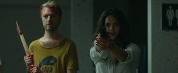 Movie still from “The Belko Experiment” (2016), directed by Greg McLean – A woman holding a gun in front of a man; Medium shot, Over the shoulder angle