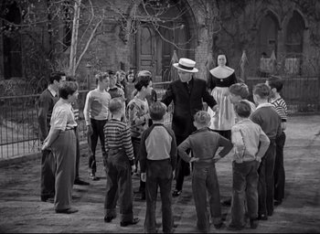 Movie still from “The Bells of St. Mary's” (1945), directed by Leo McCarey – A group of people standing around each other in front of a building; Wide shot, High angle