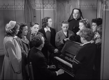 Movie still from “The Bells of St. Mary's” (1945), directed by Leo McCarey – A group of people standing around a piano; Medium shot, High angle