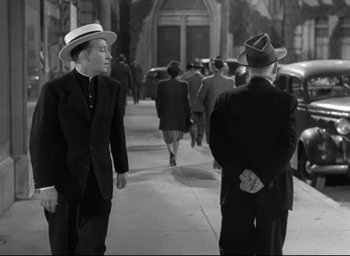 Movie still from “The Bells of St. Mary's” (1945), directed by Leo McCarey – A man in a suit and hat walking down a street; Medium shot, Over the shoulder angle