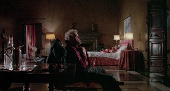 Movie still from “The Belly of an Architect” (1987), directed by Peter Greenaway – An older man sitting on a chair in a bedroom; Wide shot, Over the shoulder angle