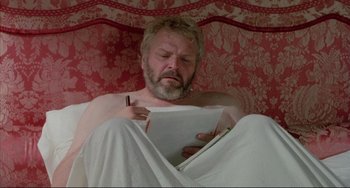 Movie still from “The Belly of an Architect” (1987), directed by Peter Greenaway – A man is reading a book in a bed; Medium shot, High angle