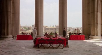 Movie still from “The Belly of an Architect” (1987), directed by Peter Greenaway – A group of people standing around a red table; Extreme Wide shot, High angle