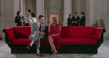 Movie still from “The Belly of an Architect” (1987), directed by Peter Greenaway – A man and a woman are sitting on a red couch; Wide shot, Low angle