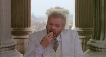 Movie still from “The Belly of an Architect” (1987), directed by Peter Greenaway – A man in a white suit is eating a piece of food; Medium shot, Low angle