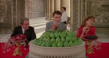 Movie still from “The Belly of an Architect” (1987), directed by Peter Greenaway – A man in a gray suit is sitting in front of a bowl of green fruit; Medium shot, High angle
