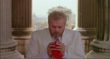 Movie still from “The Belly of an Architect” (1987), directed by Peter Greenaway – An older man in a white suit is holding a red cloth; Close Up shot, Low angle