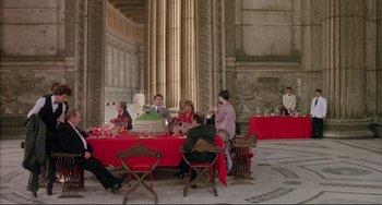 Movie still from “The Belly of an Architect” (1987), directed by Peter Greenaway – A group of people sitting around a table with a red table cloth; Extreme Wide shot, High angle