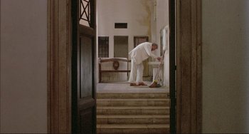 Movie still from “The Belly of an Architect” (1987), directed by Peter Greenaway – A man sweeping the steps of a building; Wide shot, Low angle