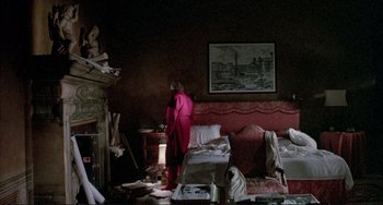 Movie still from “The Belly of an Architect” (1987), directed by Peter Greenaway – A woman standing in a living room next to a fire place; Wide shot, High angle