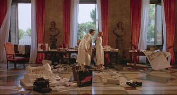Movie still from “The Belly of an Architect” (1987), directed by Peter Greenaway – A couple of people that are standing in a room; Wide shot, High angle