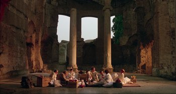 Movie still from “The Belly of an Architect” (1987), directed by Peter Greenaway – A group of people sitting around in a room; Extreme Wide shot, Low angle