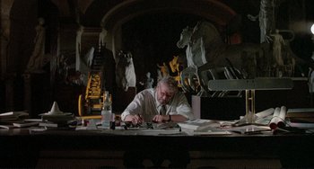 Movie still from “The Belly of an Architect” (1987), directed by Peter Greenaway – A man sitting at a table with papers on it; Wide shot, Low angle