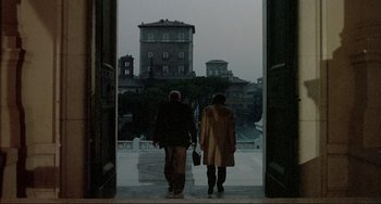 Movie still from “The Belly of an Architect” (1987), directed by Peter Greenaway – Two people are walking down the steps of a building; Wide shot, Low angle
