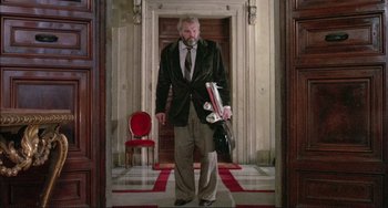 Movie still from “The Belly of an Architect” (1987), directed by Peter Greenaway – A man in a suit and tie holding a bag; Wide shot, Low angle