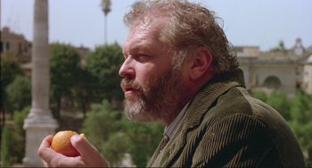 Movie still from “The Belly of an Architect” (1987), directed by Peter Greenaway – An older man with a beard eating a donut; Close Up shot, Low angle