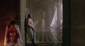 Movie still from “The Belly of an Architect” (1987), directed by Peter Greenaway – A man wearing a toga stands next to a wall; Wide shot, High angle