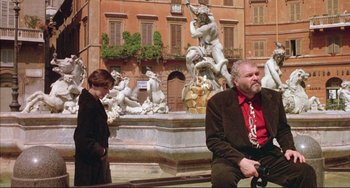 Movie still from “The Belly of an Architect” (1987), directed by Peter Greenaway – A man and a woman sitting in front of a fountain; Wide shot, Low angle