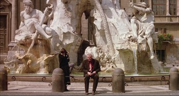Movie still from “The Belly of an Architect” (1987), directed by Peter Greenaway – A man and a woman sitting in front of a fountain; Wide shot, Low angle