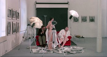 Movie still from “The Belly of an Architect” (1987), directed by Peter Greenaway – A woman standing on a red couch in front of a camera; Wide shot, High angle