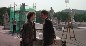 Movie still from “The Belly of an Architect” (1987), directed by Peter Greenaway – Two men are standing next to each other on the street; Medium shot, Over the shoulder angle