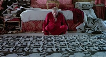 Movie still from “The Belly of an Architect” (1987), directed by Peter Greenaway – A man sitting on the floor in front of pictures; Medium shot, Overhead angle