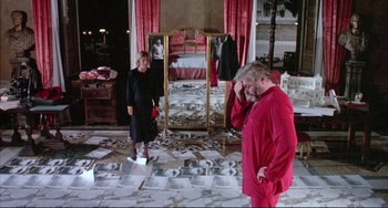 Movie still from “The Belly of an Architect” (1987), directed by Peter Greenaway – Two people in a room with a bed and a mirror; Wide shot, High angle