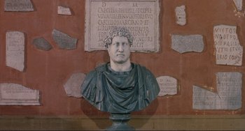 Movie still from “The Belly of an Architect” (1987), directed by Peter Greenaway – A bust of a man in front of a brick wall; Close Up shot, High angle