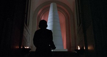 Movie still from “The Belly of an Architect” (1987), directed by Peter Greenaway – A woman standing in front of a large white pillar; Wide shot, Low angle