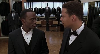 Movie still from “The Best Man” (1999), directed by Malcolm D. Lee – Two men in tuxedos talking to each other in front of suits; Medium shot, Over the shoulder angle