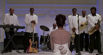 Movie still from “The Best Man” (1999), directed by Malcolm D. Lee – A woman in a white dress is playing a musical instrument; Wide shot, Over the shoulder angle
