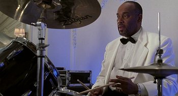 Movie still from “The Best Man” (1999), directed by Malcolm D. Lee – A man in a white tuxedo playing drums; Medium shot, Low angle