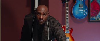 Movie still from “The Best Man Holiday” (2013), directed by Malcolm D. Lee – A bald man with a guitar in front of him; Medium shot, Over the shoulder angle