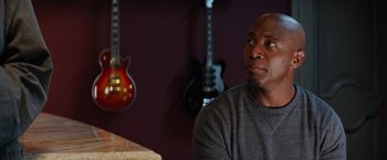Movie still from “The Best Man Holiday” (2013), directed by Malcolm D. Lee – A man sitting in front of a table with guitars; Close Up shot, Over the shoulder angle