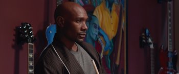 Movie still from “The Best Man Holiday” (2013), directed by Malcolm D. Lee – A man standing in front of a painting holding a drum stick; Medium shot, Over the shoulder angle