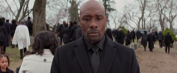 Movie still from “The Best Man Holiday” (2013), directed by Malcolm D. Lee – A man in a black suit and black tie standing in front of a group of people; Close Up shot, High angle