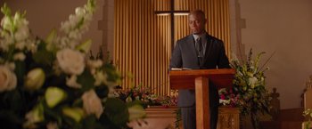 Movie still from “The Best Man Holiday” (2013), directed by Malcolm D. Lee – A man standing at a podium in front of flowers; Medium shot, Low angle