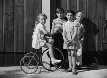 Movie still from “The Best Years of Our Lives” (1946), directed by William Wyler – A group of children standing next to each other next to a bicycle; Wide shot, High angle