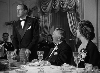 Movie still from “The Best Years of Our Lives” (1946), directed by William Wyler – A man in a tuxedo standing at a dinner table; Medium shot, Over the shoulder angle
